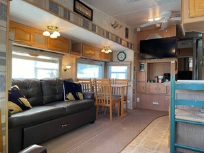 Interior de una caravana compacta con kitchenette, una zona de comedor y una sala de estar con sofá y sillones.