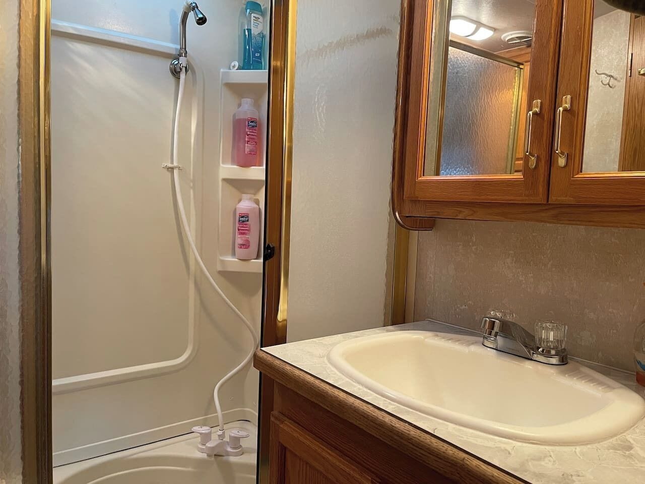 A bathroom with a shower, a sink, and wooden cabinets.