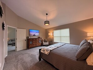 A bedroom with a bed, a dresser, a television, and a window with blinds.