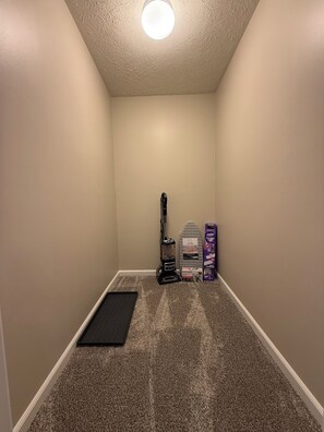 A carpeted room with a vacuum cleaner, ironing board, and ironing board cover.
