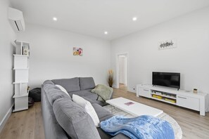 En moderne stue med en grå sofa, et hvidt tv-møbel og et fladskærms-tv.