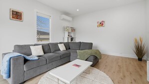 A modern living room with a grey sectional sofa, a white coffee table, and a bookshelf. - Apple Court Retreat – 3 Bedroom – Access to Huon River (Huonville)