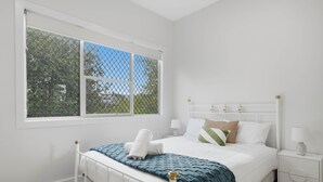 A bedroom with a white bed, a window with a view of trees, and a bedside table with a lamp. - Apple Court Retreat – 3 Bedroom – Access to Huon River (Huonville)