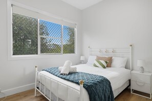 Ein Schlafzimmer mit einem weißen Bett, einem Fenster mit Blick auf Bäume und einem Nachttisch mit einer Lampe.