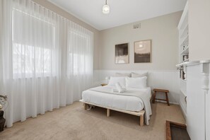 A bedroom with a bed, a bedside table, a nightstand, a window with sheer curtains, and two wall-mounted pictures. - Cottage on Quayle - 3 Bedroom in Sandy Bay (Sandy Bay)