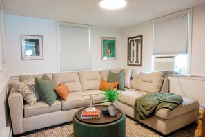 A living room with a beige sofa, a round coffee table, and a green plant. - Retro Luxe Suite, Downtown Manchester near Hartford Sleeps 4! New! (Manchester)
