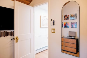 Ein Flur mit einer weißen Tür, einem an der Wand montierten Lichtschalter und einem kleinen Schrank mit Plattenspieler.