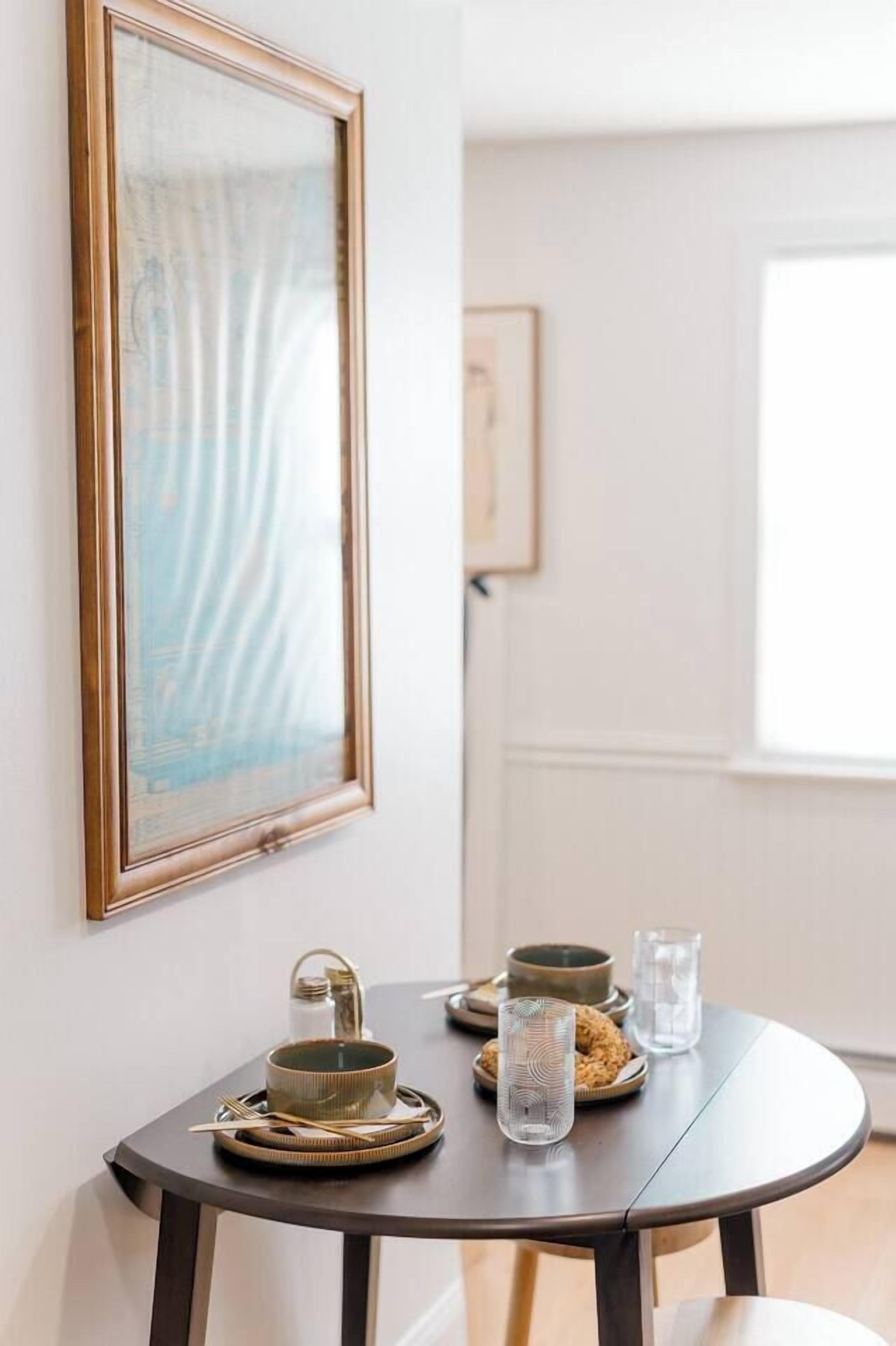 A dining table with a framed artwork, a bowl, a glass, and a candle holder.