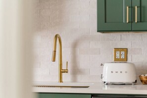 A kitchen with a gold faucet, white tiled backsplash, green cabinets, and a white toaster. - Retro Luxe Suite, Downtown Manchester near Hartford Sleeps 4! New! (Manchester)