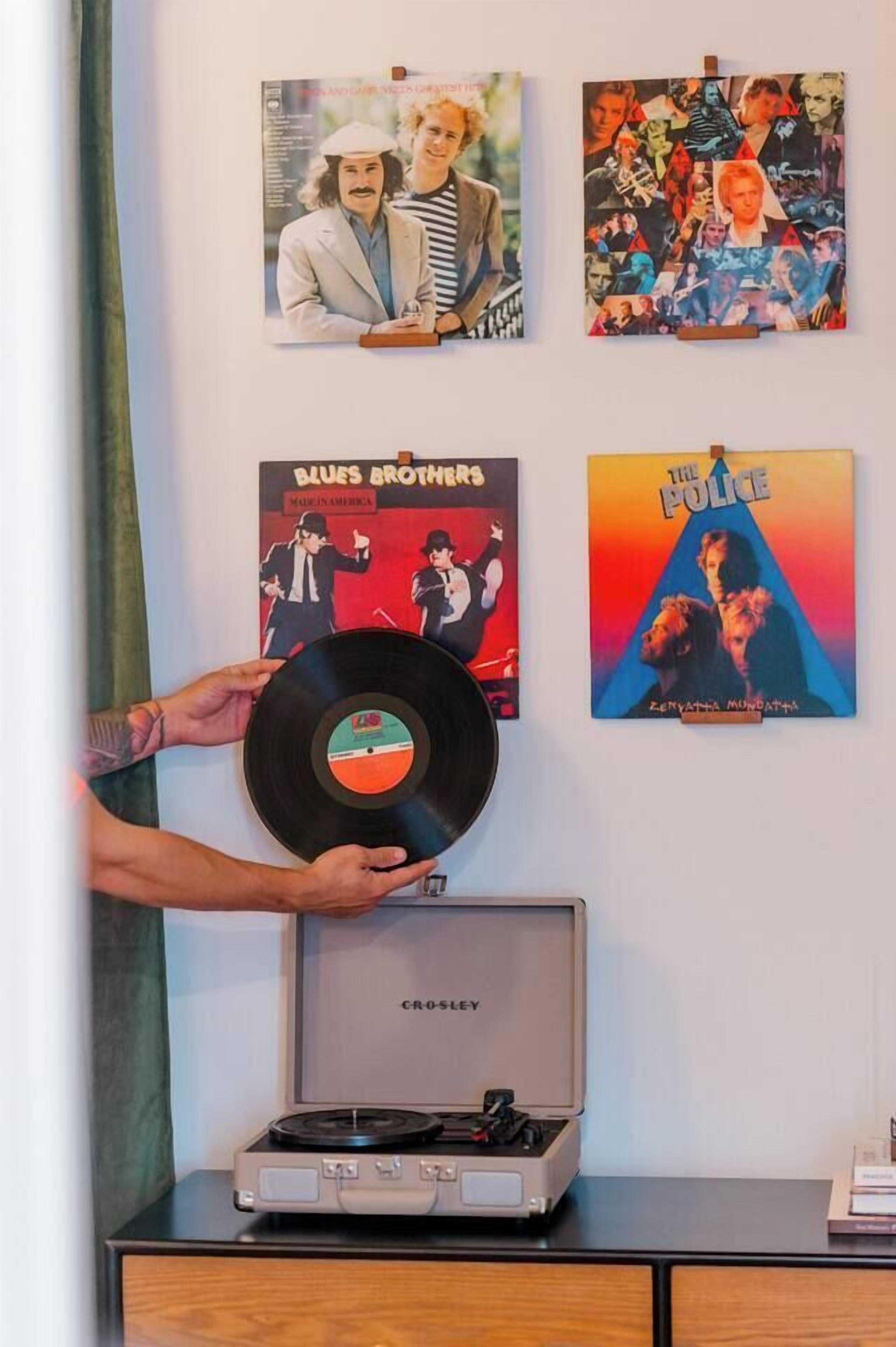 Eine Schallplatte auf einem Plattenspieler, dazwischen Alben an der Wand.