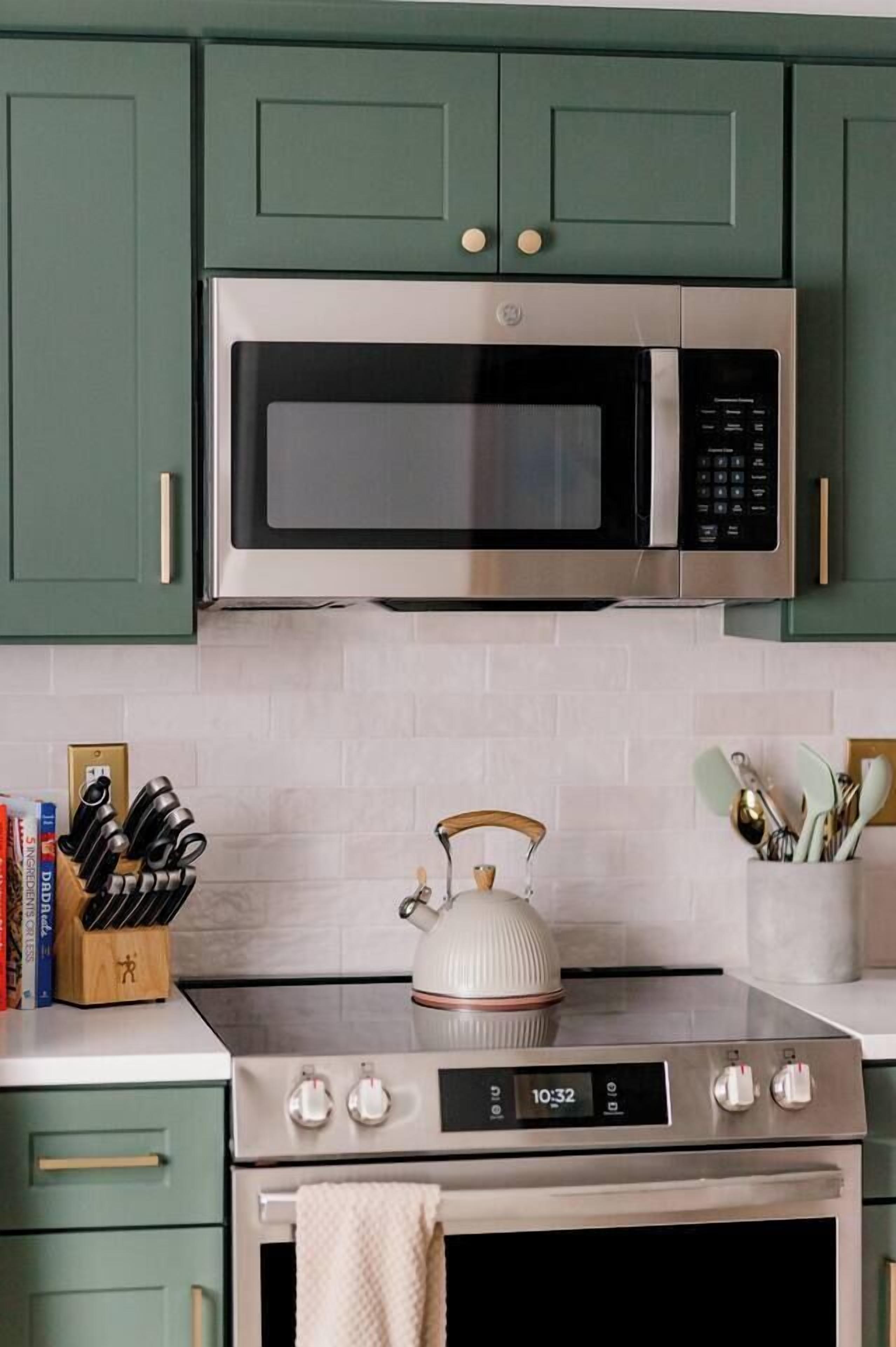 A kitchen with a stainless steel microwave, a stove, and a kettle.