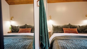 A mirrored view of a bedroom with a wooden ceiling, a bed with a quilted bedspread, two pillows, and bedside lamps. - Retro Luxe Suite, Downtown Manchester near Hartford Sleeps 4! New! (Manchester)