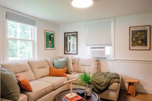 Un salon avec un canapé beige, une table basse sur laquelle sont posés des livres et une plante, et un petit tabouret en bois.
