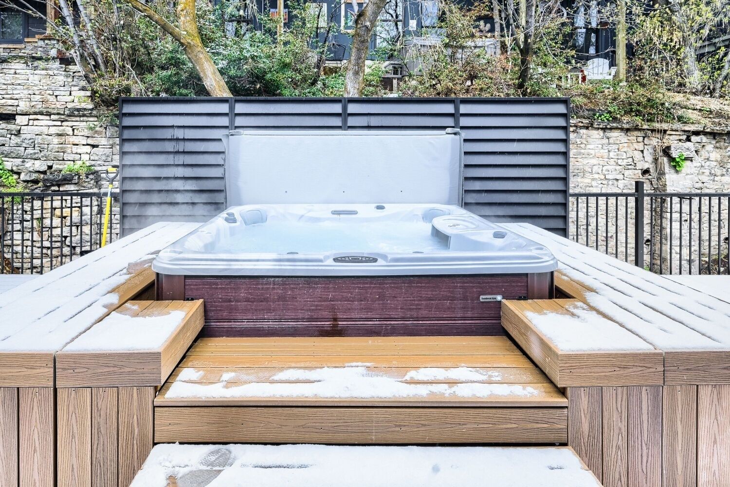 A hot tub with a wooden deck and stone wall backdrop.