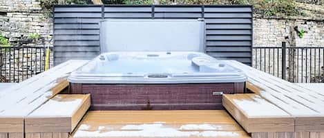 Een hottub met een houten terras en een achtergrond van een stenen muur.
