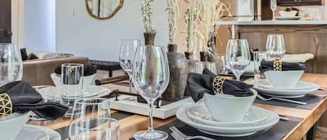 A dining table set with plates, glasses, and cutlery, with a vase of dried flowers in the center.