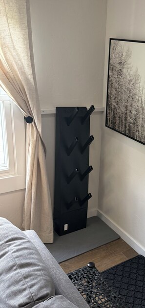 Ein Zimmer mit einem Bett, einer schwarzen Kommode mit Haken, einem gerahmten Bild an der Wand und einem Fenster mit Vorhängen.