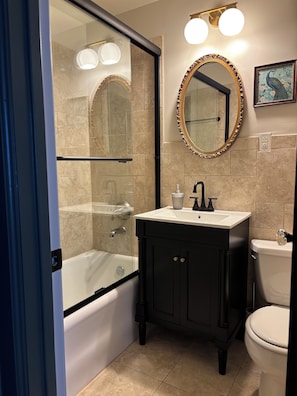 Une salle de bain avec une douche à parois de verre, des toilettes blanches, un meuble-lavabo noir et un miroir doté d’un cadre décoratif.