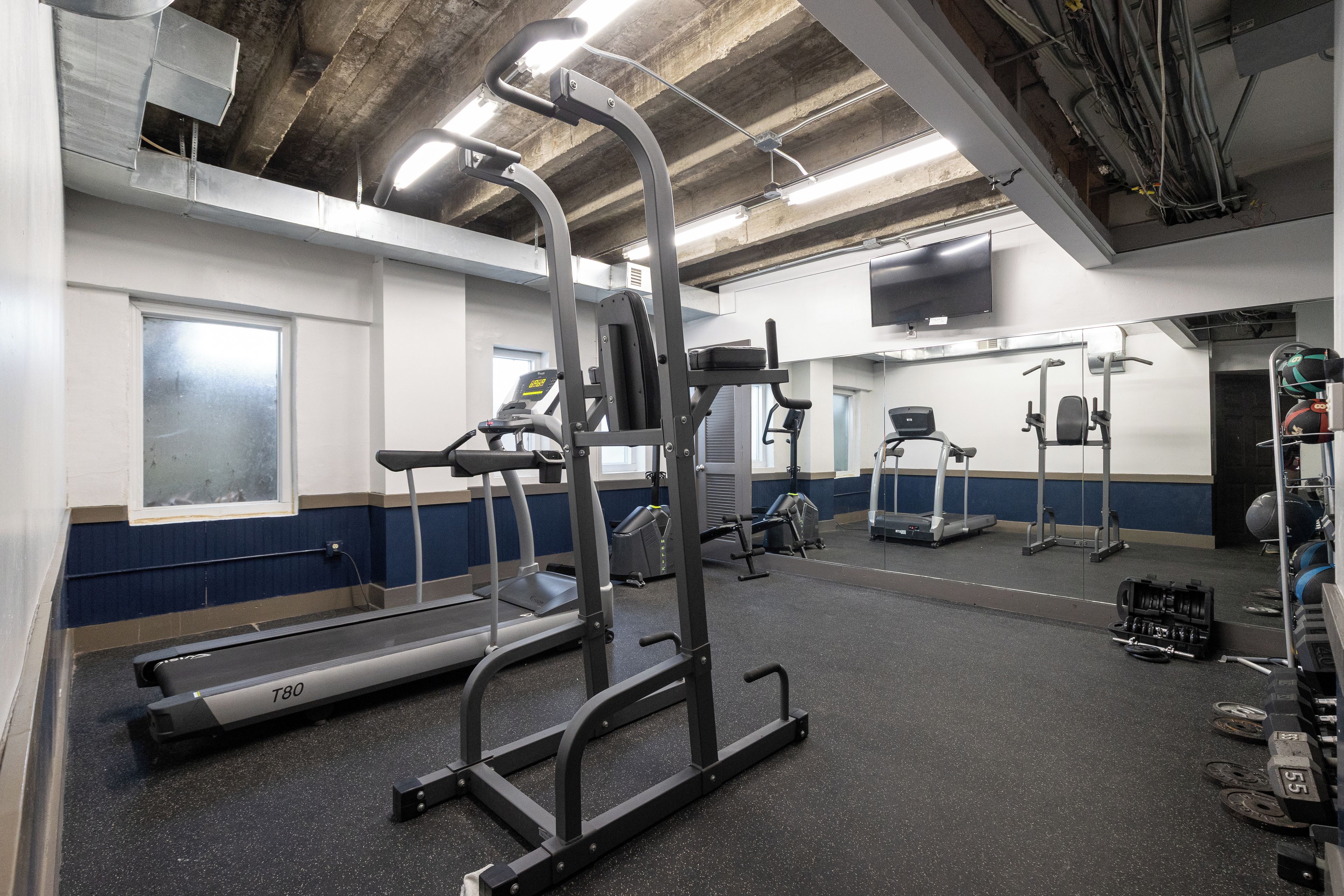 Ein Fitnessstudio mit Laufbändern, Kraftgeräten und einem Fernseher an der Wand.