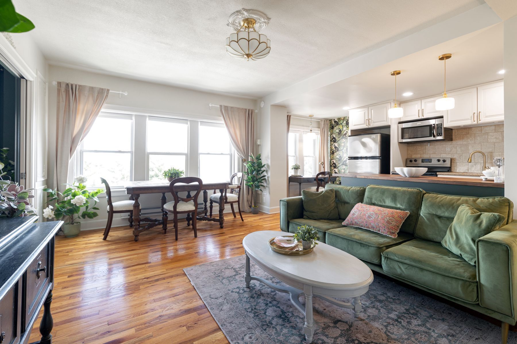 A modern living room with a green sofa, a dining table with chairs, and a kitchen area with appliances.