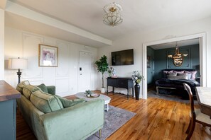 A living room with a green sofa, a coffee table, a lamp, and a TV on the wall.