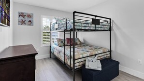 A bunk bed with a patterned bedspread, a desk, and a window with blinds.
