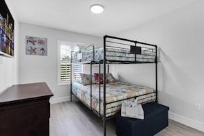 A bunk bed with a patterned bedspread, a desk, and a window with blinds.