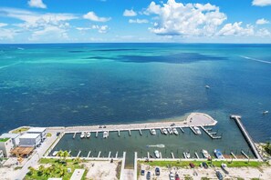 A marina with boats docked, a pier extending into the water, and a building with a green roof.