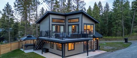 A modern two-story house with a balcony, large windows, and a deck area.
