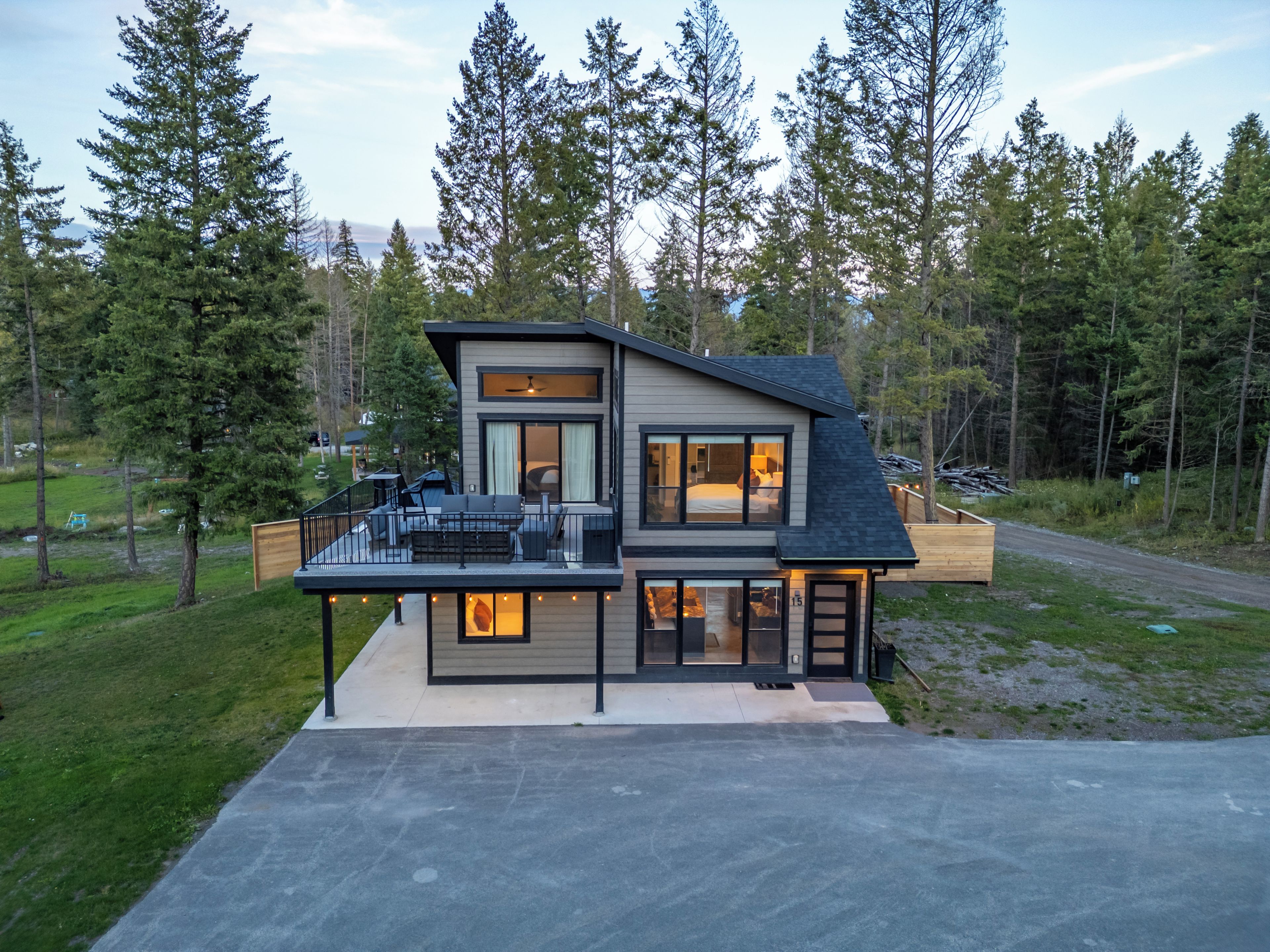 A modern two-story house with a balcony, large windows, and a view of a forest.