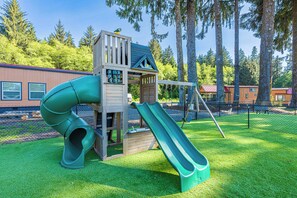 Un'area giochi con uno scivolo e una struttura per arrampicarsi, circondata da alberi e un edificio sullo sfondo.
