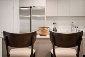 Une cuisine moderne avec deux chaises en bois foncé, un comptoir blanc et un réfrigérateur en acier inoxydable.