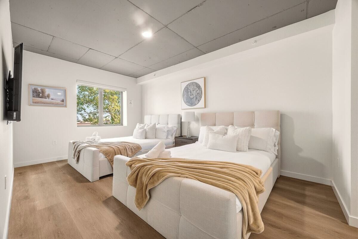 A bedroom with two beds, a large window, and a ceiling fan.