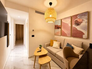 Ein modernes Wohnzimmer mit einer Couch, einem Couchtisch und einer Pendelleuchte. An der Wand befinden sich drei gerahmte Bilder.