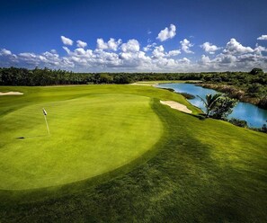 Campo de golf con un mástil de bandera, obstáculos acuáticos y cielo despejado.