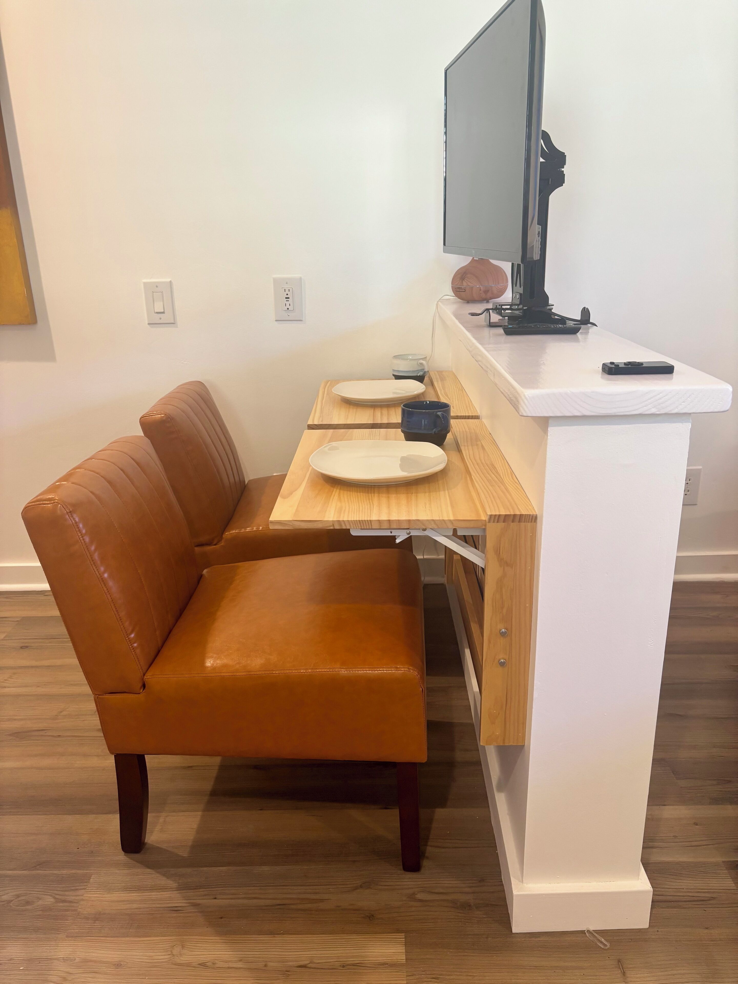 A compact living space with a brown leather couch, a small wooden table with a white countertop, a television, and a few items on the table.