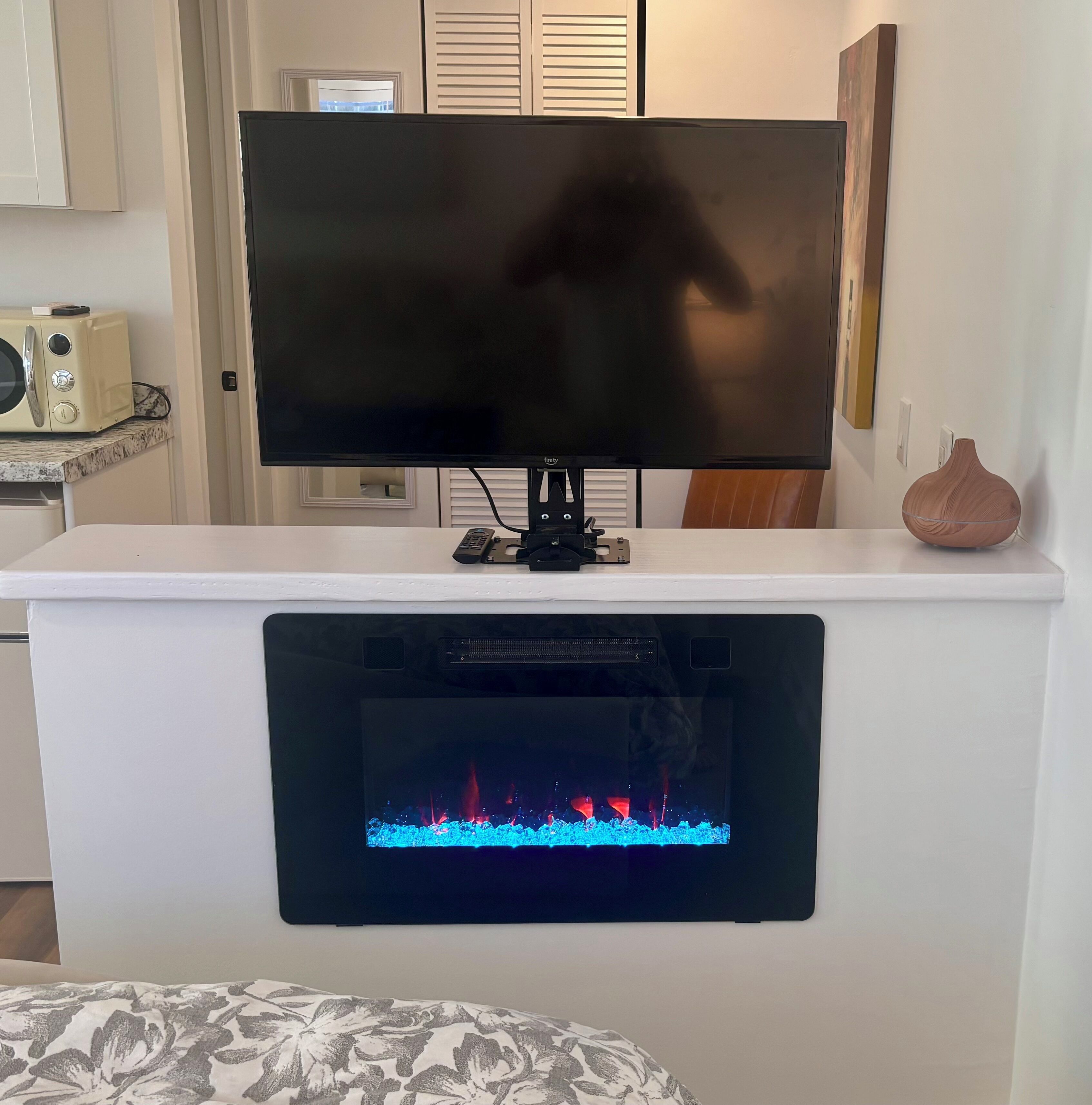A flat-screen TV mounted on a white wall above a fireplace with a game console below.