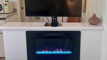 A flat-screen TV mounted on a white wall above a fireplace with a game console below.