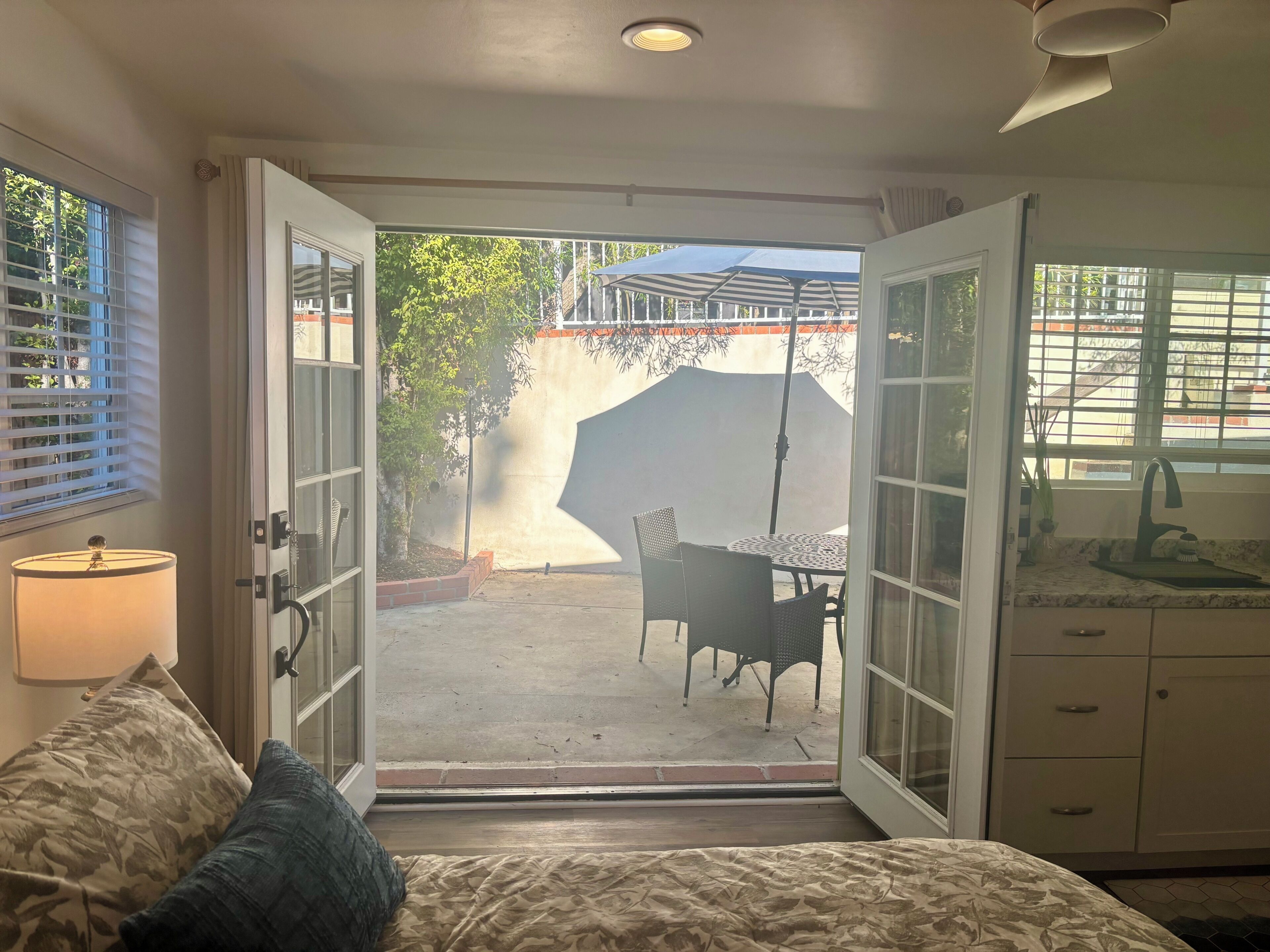 Une chambre à coucher comprenant un lit, une table de chevet, une lampe et donnant sur une terrasse extérieure avec une table et des chaises.