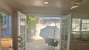 Une chambre à coucher comprenant un lit, une table de chevet, une lampe et donnant sur une terrasse extérieure avec une table et des chaises.