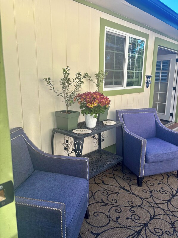 A room with two upholstered chairs, a small table with a vase of flowers, and a window with shutters.