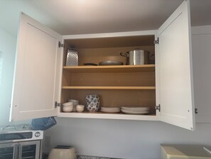 A kitchen with a white cabinet containing a grater, pots, and plates.