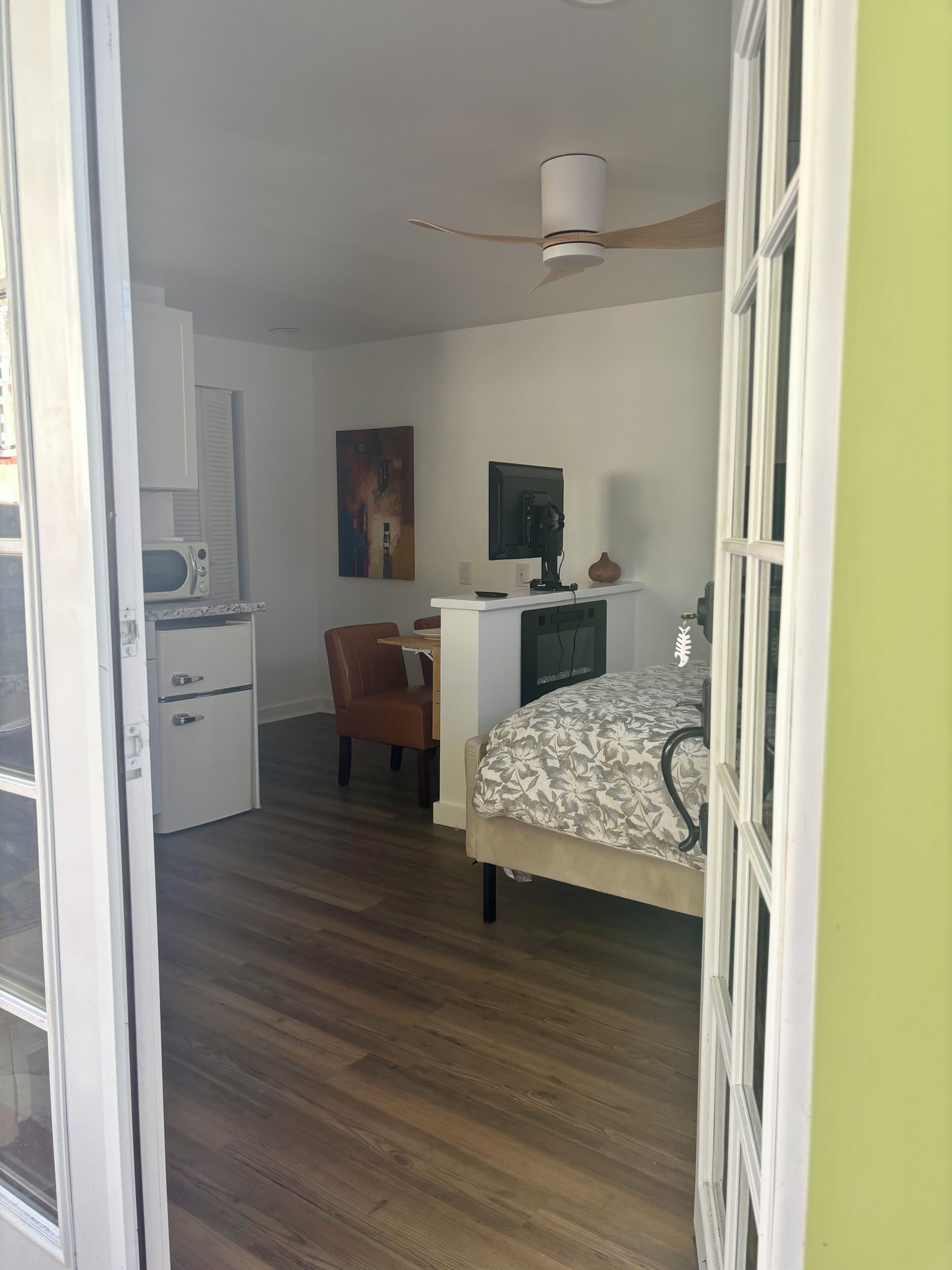 A room with a bed, a desk, a chair, a ceiling fan, and a microwave.