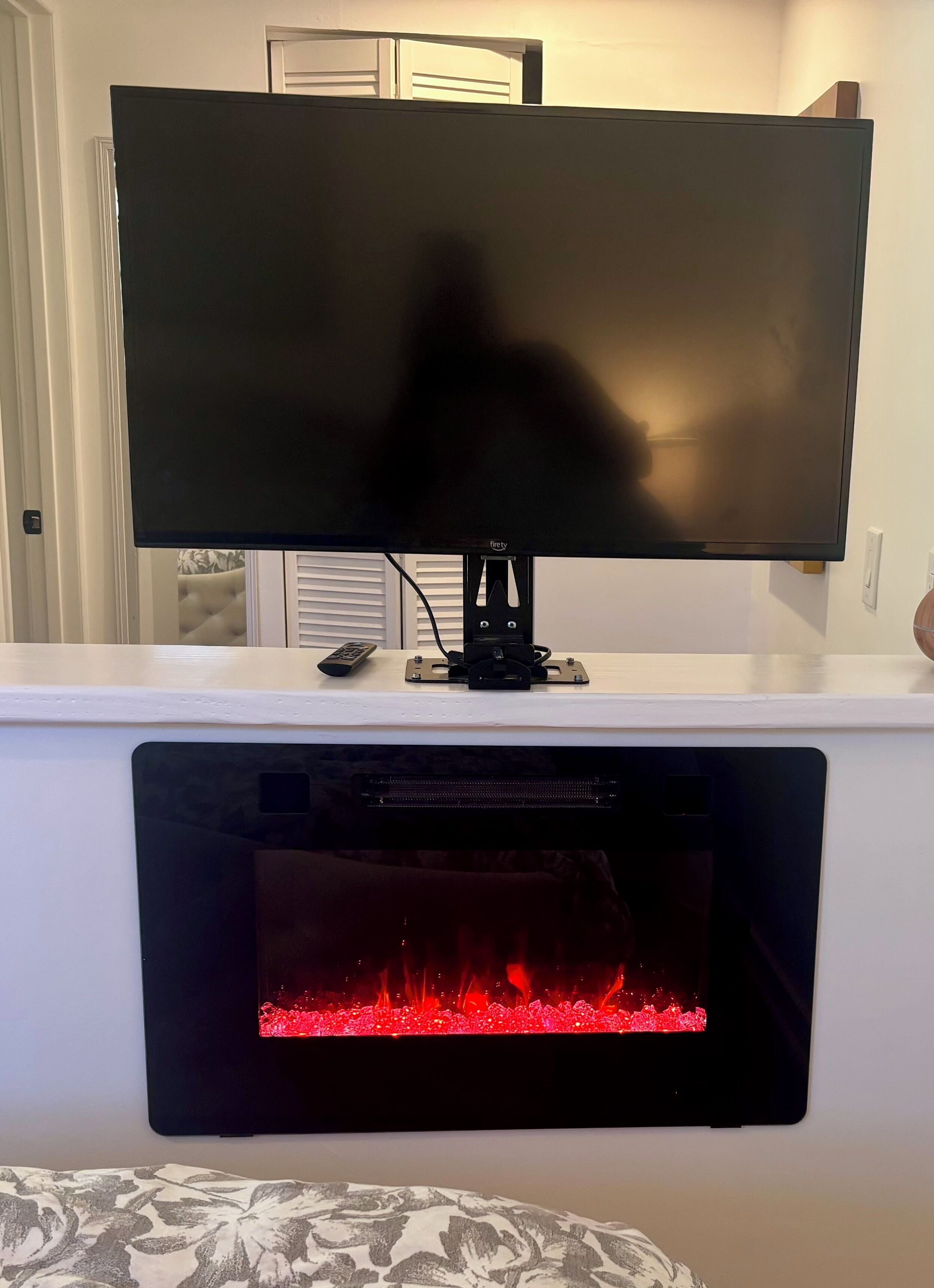 Ein Flachbildfernseher an einer weißen Wand über einem Kamin mit sichtbarem Feuer.