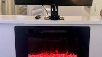 Ein Flachbildfernseher an einer weißen Wand über einem Kamin mit sichtbarem Feuer.