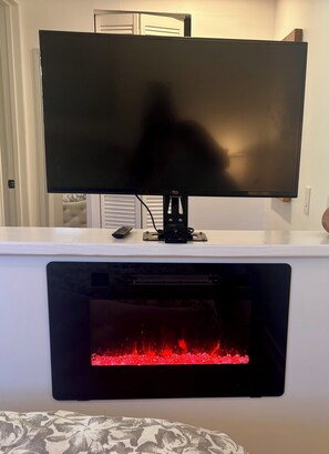 A flat-screen TV mounted on a white wall above a fireplace with a visible fire.