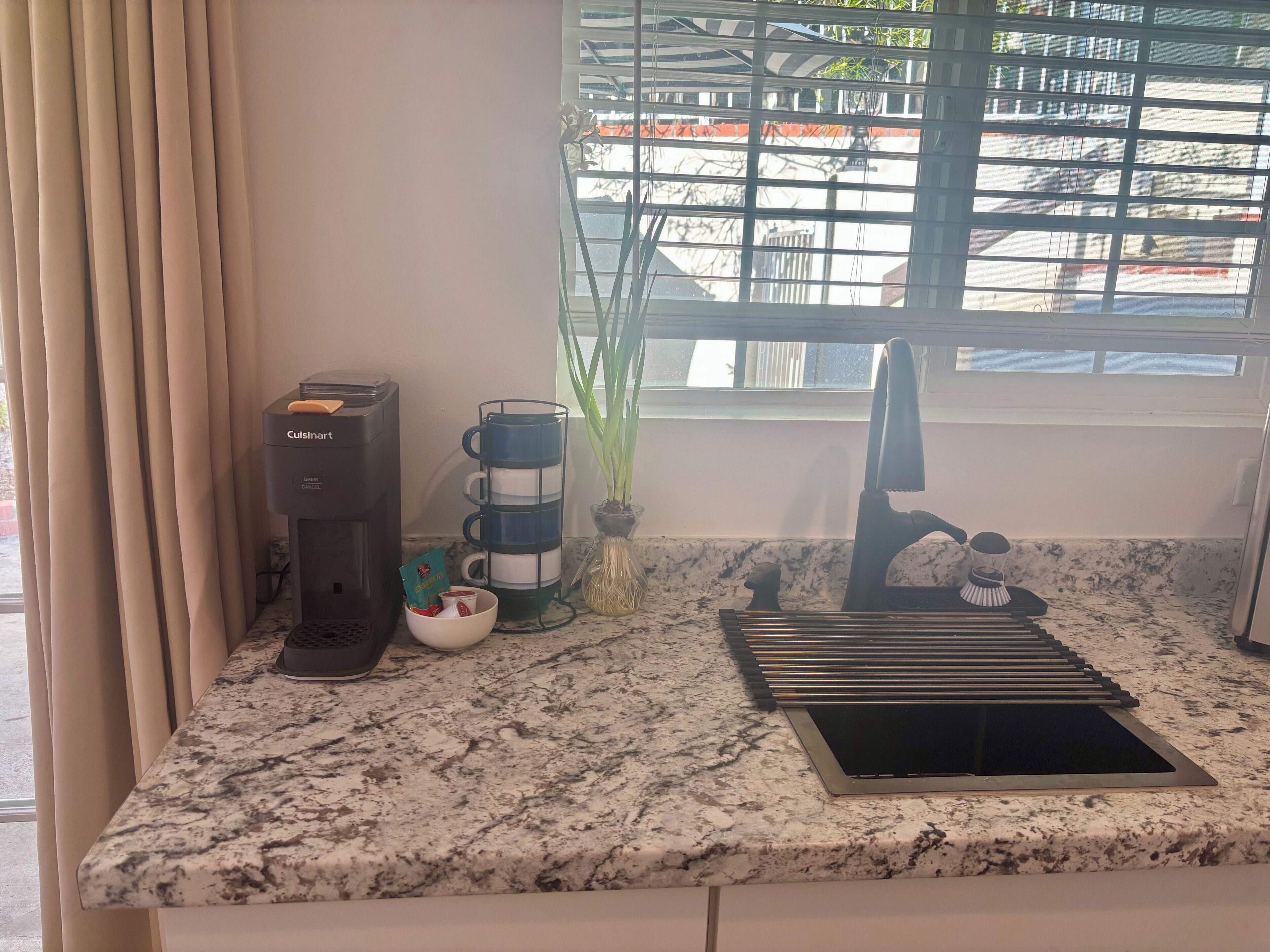 Eine Küchenarbeitsplatte mit Kaffeemaschine, Tasse, Pflanze und Spüle.