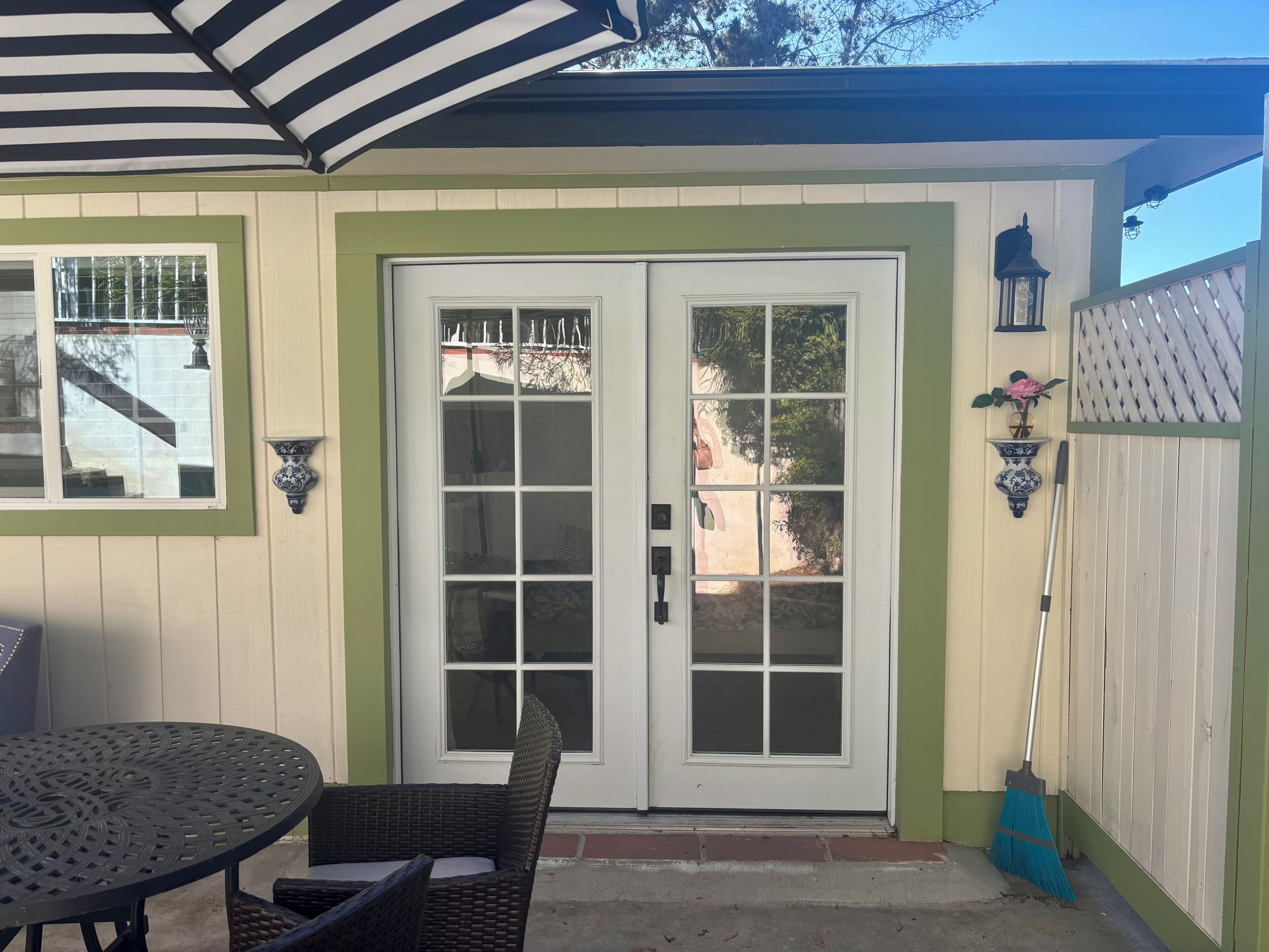 A patio with a table and chairs, a white door with glass panels, and a blue broom leaning against the wall.