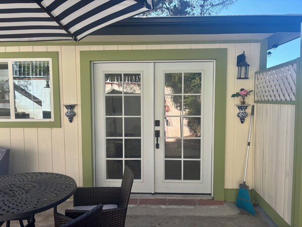 A patio with a table and chairs, a white door with glass panels, and a blue broom leaning against the wall.