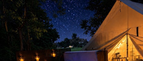 A hot tub with candles, a fire feature, and a tent in a forested area.